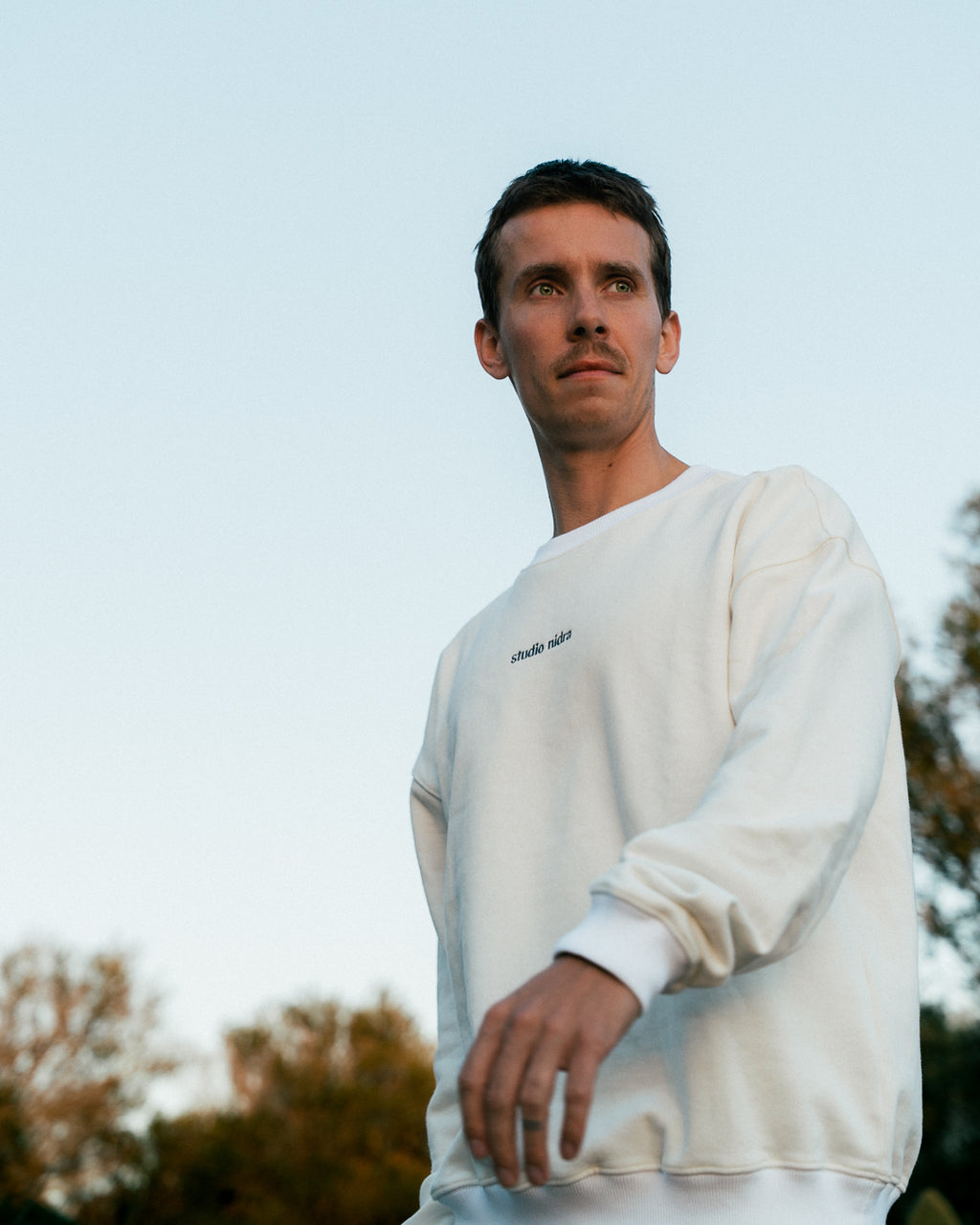 Man wearing the organic cotton crewneck sweatshirt with Studio Nidra embroidery, standing outdoors against the blue sky of Mallorca